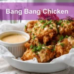 Bang Bang Chicken golden crispy pieces drizzled with sauce and fresh herbs on white cloth