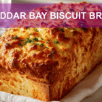CHEDDAR BAY BISCUIT BREAD loaf on white napkin, warm light, golden crust, glass of water beside.