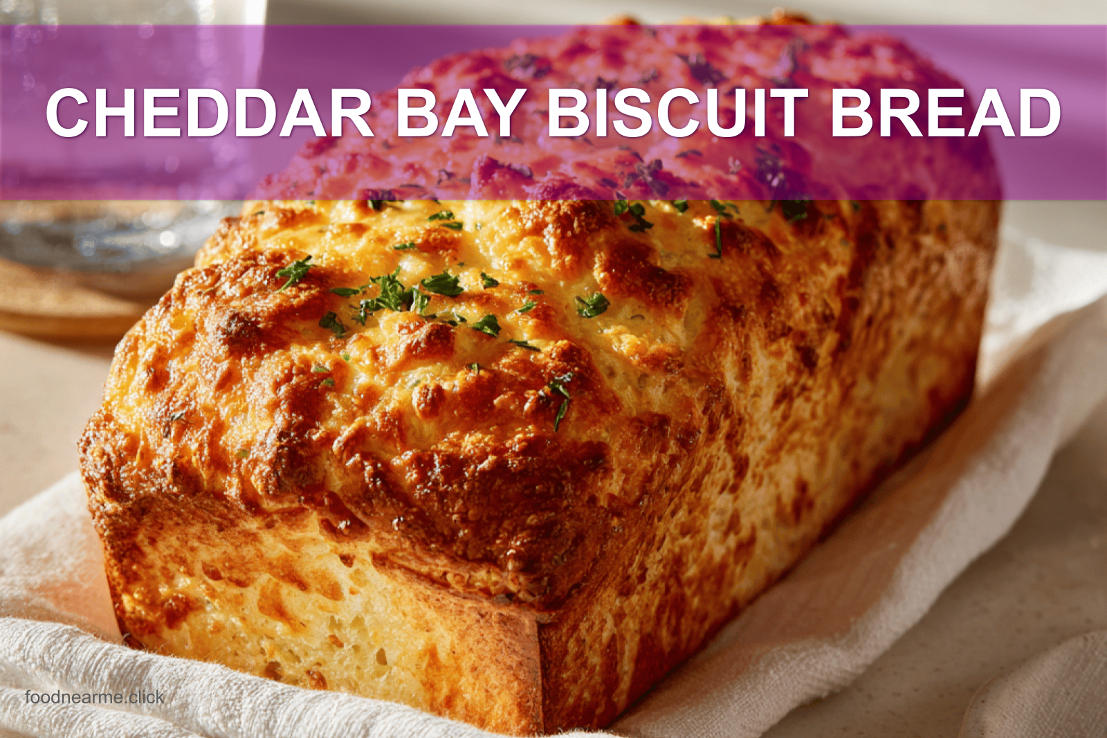 CHEDDAR BAY BISCUIT BREAD loaf on white napkin, warm light, golden crust, glass of water beside.