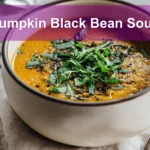 Pumpkin Black Bean Soup garnished with fresh herbs, served on a white napkin with a glass of water.
