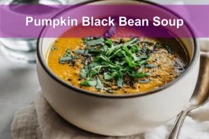Pumpkin Black Bean Soup garnished with fresh herbs, served on a white napkin with a glass of water.