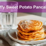 Fluffy Sweet Potato Pancakes stacked with melted butter and syrup on white napkin beside clear water glass