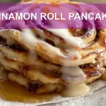 CINNAMON ROLL PANCAKES stacked with maple syrup and delicate white cheese glaze on white cloth