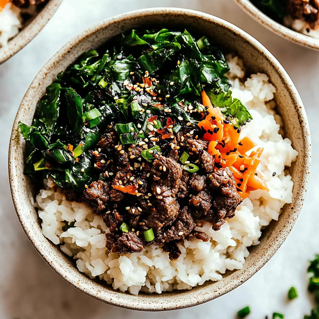 Korean beef bulgogi rice bowls served in white bowl with wilted spinach, julienned carrots, and sesame seeds
